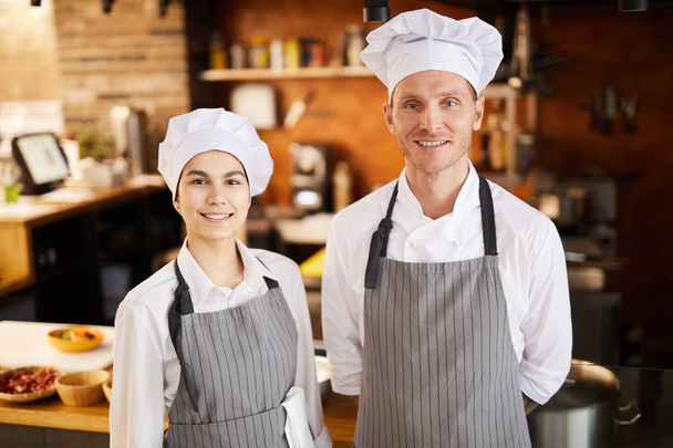 Portrait taille haute de deux cuisiniers professionnels posant dans la cuisine du restaurant souriant à la caméra, espace de copie
 - Photo, image