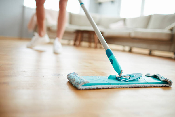 Close-up of unrecognizable woman using mop with microfiber pad while cleaning parquet floor in living room - Foto, Imagen