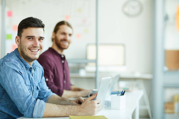 Iloinen nuori johtaja hammas hymy ja hänen kollegansa casualwear katselee sinua työpaikalla
 - Valokuva, kuva