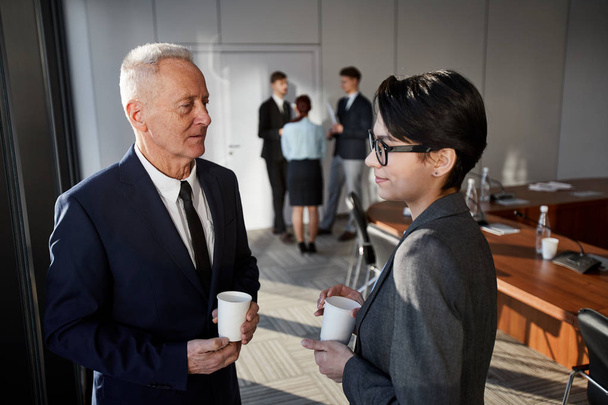 Taillenhoch Porträt eines leitenden Geschäftsmannes, der während einer Kaffeepause im Konferenzraum mit einer jungen Frau spricht, Kopierraum - Foto, Bild