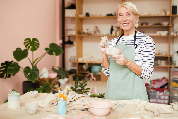 Retrato de cintura hacia arriba de una artista sonriente mirando a la cámara mientras posa en un taller de cerámica, espacio para copiar
 - Foto, Imagen