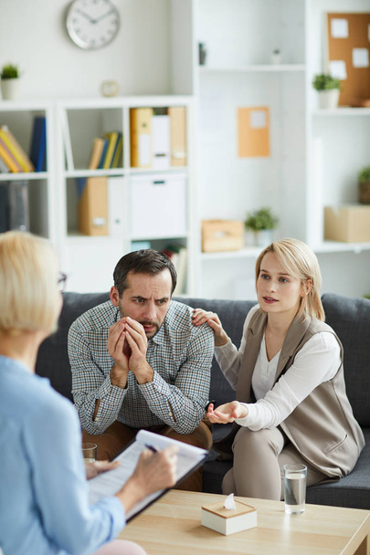 Blonde young woman explaining something to counselor while sitting on couch next to her husband - Photo, image