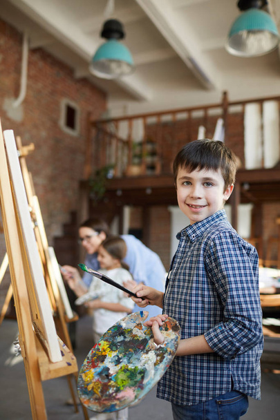 Πορτρέτο του χαμογελαστά αγόρι ζωγραφική εικόνα σε καβαλέτο στην κλάση τέχνης και κρατώντας παλέτα, αντίγραφο χώρου - Φωτογραφία, εικόνα