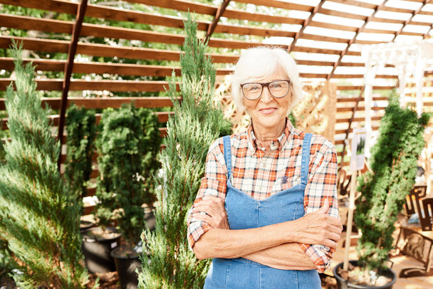 Portrait taille haute de femme âgée heureuse posant dans le jardin debout avec les bras croisés et regardant la caméra, l'espace de copie
 - Photo, image