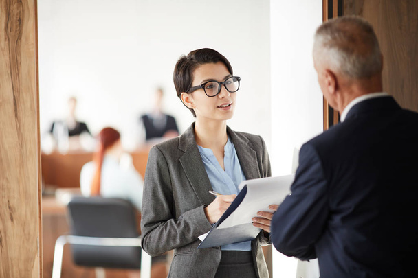 Waist up portrait of young businesswoman holding clipboard asking questions while talking to boss or business coach, copy space - Photo, Image