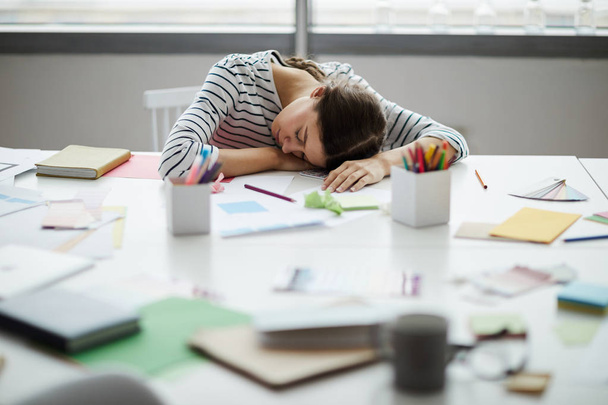 Portret van hedendaagse jonge vrouw slapen op tafel op het werk, kopieer ruimte - Foto, afbeelding