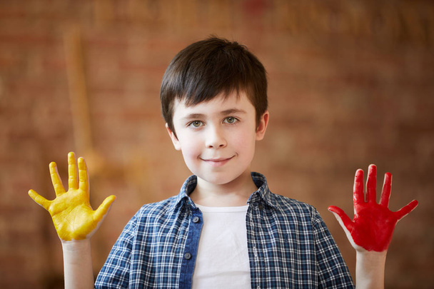 Портрет милого маленького хлопчика, який показує руки розфарбовані фарбою і дивиться на камеру, малюнок пальців і концепцію творчості
 - Фото, зображення