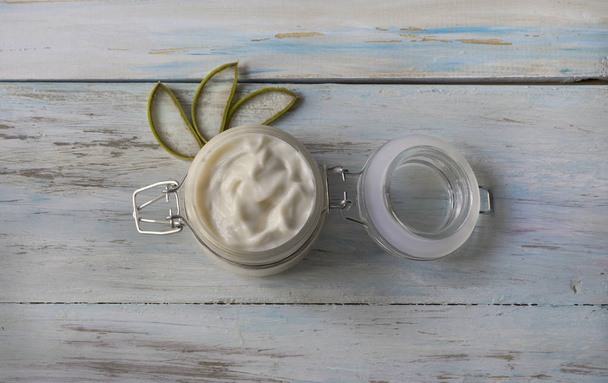 Homemade Aloe Vera cream in a glass jar, with cut aloe leaves on a light wood background - Photo, Image