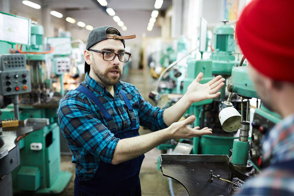 Portrait d'un ouvrier barbu pointant du doigt les unités de la machine tout en parlant au stagiaire en atelier, espace de copie
 - Photo, image