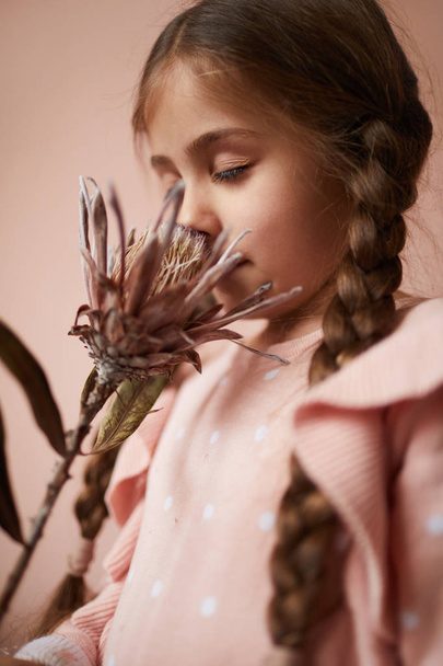 Muotokuva söpö pieni tyttö hajuinen eksoottinen kukka pölyinen vaaleanpunainen tausta
 - Valokuva, kuva
