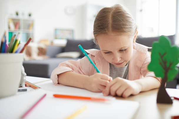 Portrait of cute girl doing homework at home learning to write with pencil, copy space - Photo, Image