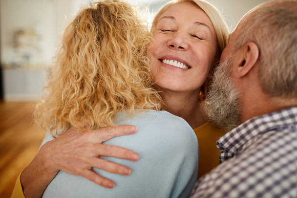 Happy excited mature woman with closed eyes embracing friends while welcoming them to home - Fotoğraf, Görsel