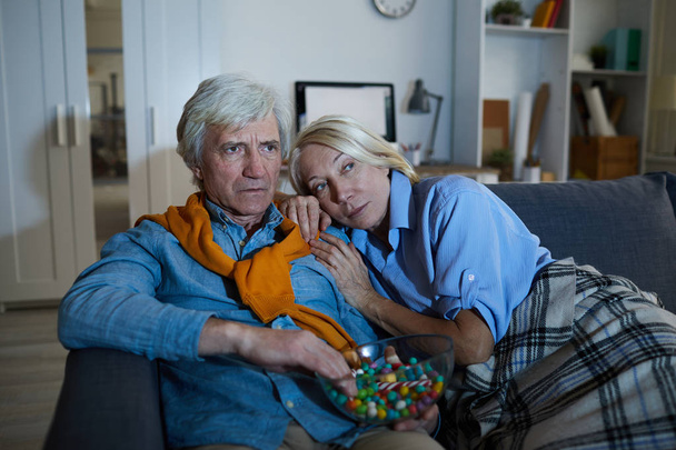 Portrait de couple d'âge mûr contemporain regardant la télévision dans l'obscurité à la maison assis sur un canapé confortable, espace de copie
 - Photo, image