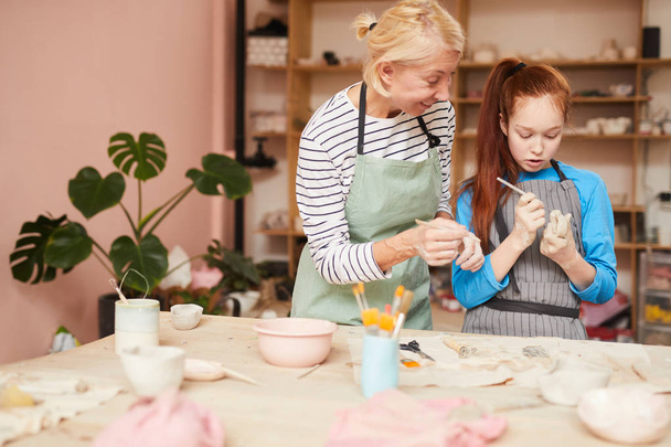 Портрет женщины-учителя искусства, помогающей девочке-подростку создавать керамику ручной работы в классе керамики, копировальное пространство
 - Фото, изображение