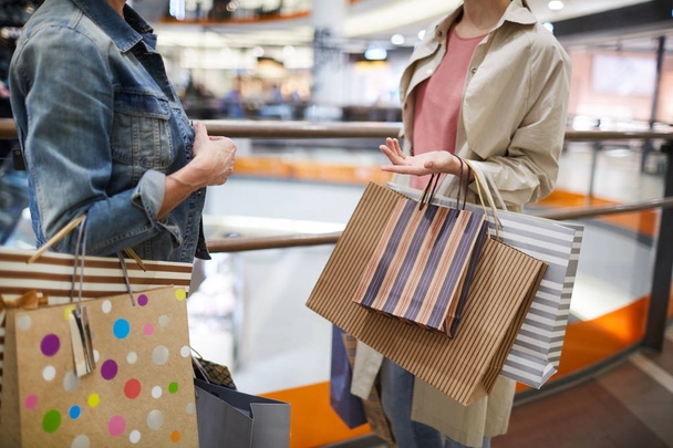 Nahaufnahme moderner Frauen in lässigen Outfits, die in der Lobby eines Einkaufszentrums stehen und Hände gestikulieren, während sie über Einkäufe diskutieren - Foto, Bild