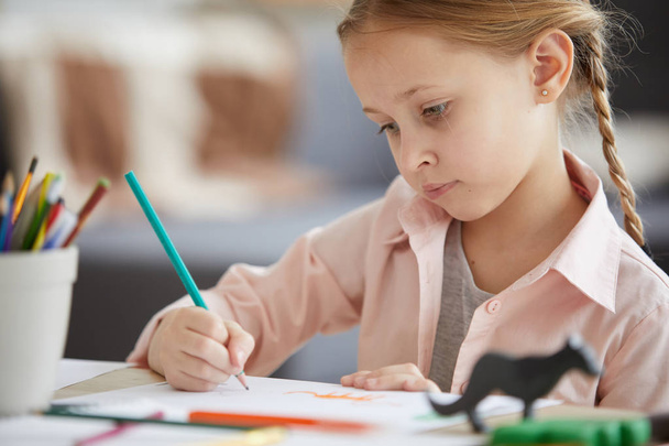 Portret van schattig meisje tekening Foto's zittend aan tafel alleen thuis, kopieer ruimte - Foto, afbeelding