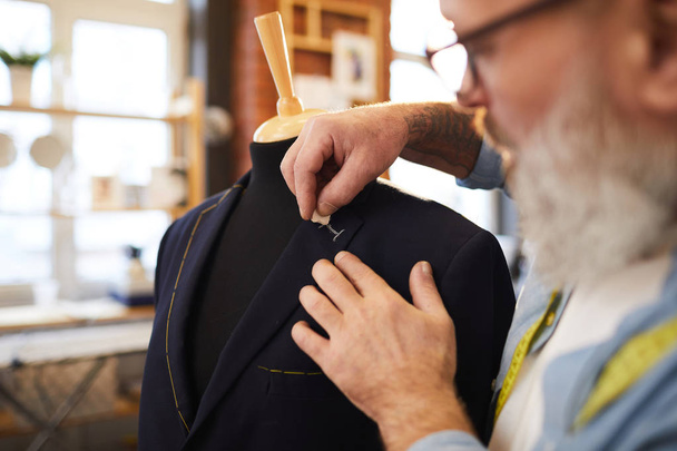 Starszy krawiec linia rysunkowy na guziki na płaszczu podczas pracy nad zamówieniem klienta w krawieckim sklepie - Zdjęcie, obraz