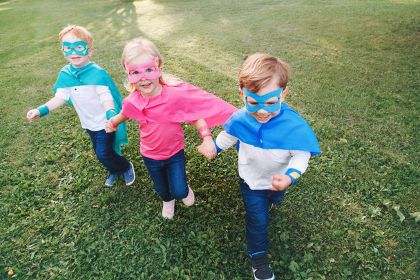 Cute adorable preschool Caucasian children playing superheroes. Three kids friends having fun together and running outdoors in park. Happy active childhood and friendship concept. - Photo, Image