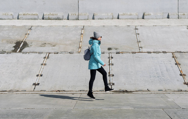 Profile view: a girl in a blue jacket is hopping on a concrete surface. - Photo, image