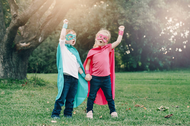 Cute adorable preschool Caucasian children boy and girl playing superheroes. Two kids friends having fun together outdoors in park. Happy active childhood and friendship concept.  - Photo, image