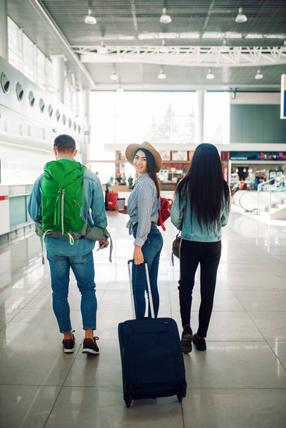 Trzech turystów z bagażem wewnątrz lotniska, widok z powrotem. Pasażerowie z bagażem w terminalu lotniczym, Happy Journey, podróży letniej - Zdjęcie, obraz
