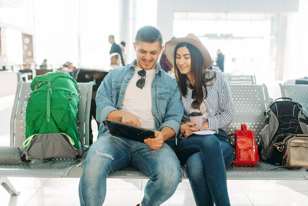 Влюбленная пара с рюкзаком ждет вылета в аэропорту. Пассажиры с багажом в аэровокзале, счастливого путешествия, летних путешествий
 - Фото, изображение