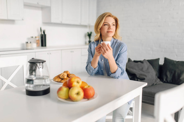 Mujer feliz bebe café con leche, desayuno en la cocina. Persona femenina en casa por la mañana, alimentación saludable y estilo de vida
 - Foto, Imagen