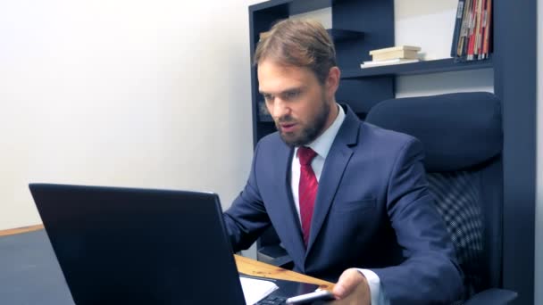 close-up. Businessman using mobile smartphone and smiling, while working on laptop computer in office. - Materiał filmowy, wideo