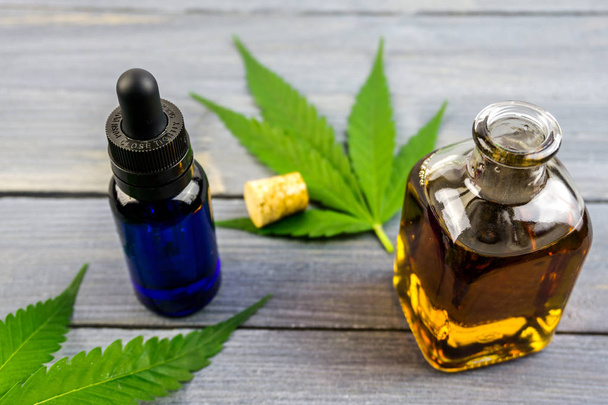 Hennep bladeren op houten achtergrond, cannabisolie extracten in flessen - Foto, afbeelding