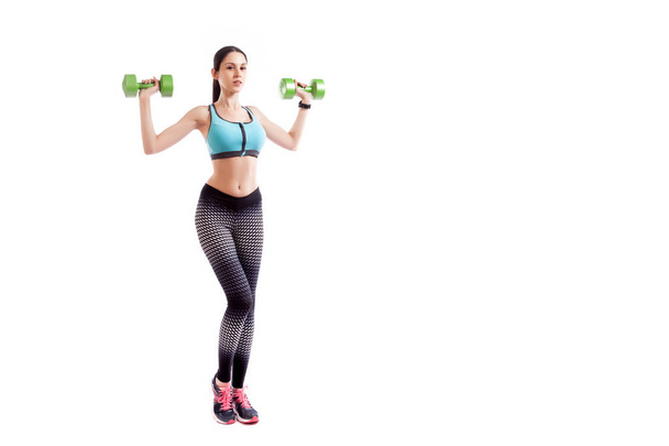 Young sportive woman fitness model brunette doing exercise with dumbbell on biceps on white isolated background. Fit girl living an active lifestyle - Photo, Image