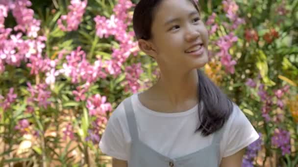 Happy Asian girl enjoying blooming flowers in summer garden at sunny day, Slow motion shot - Imágenes, Vídeo