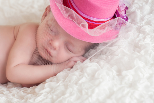 Un retrato de una niña recién nacida dormida que lleva un sombrero de ala rosa con una red en la cara.
. - Foto, imagen