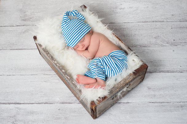 Newborn baby wearing blue and white striped pajamas and sleeping in a vintage, wooden, soda pop crate. - Photo, Image