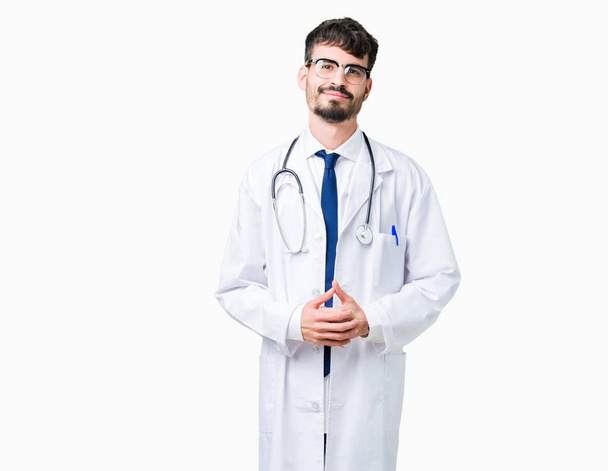 Young doctor man wearing hospital coat over isolated background Hands together and fingers crossed smiling relaxed and cheerful. Success and optimistic - Photo, image