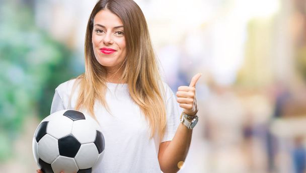 Jonge mooie vrouw houdt van voetbal over geïsoleerd achtergrond blij met de grote glimlach doen ok teken, duim omhoog met vingers, uitstekende teken - Foto, afbeelding