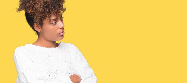 Hermosa joven afroamericana americana vistiendo suéter de invierno sobre fondo aislado sonriendo mirando a un lado con los brazos cruzados convencida y confiada
 - Foto, Imagen