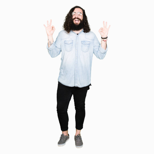 Jonge hipster man met lange haren en baard dragen van een bril ontspannen en lachend met ogen gesloten doen meditatie gebaar met vingers. Yoga concept. - Foto, afbeelding