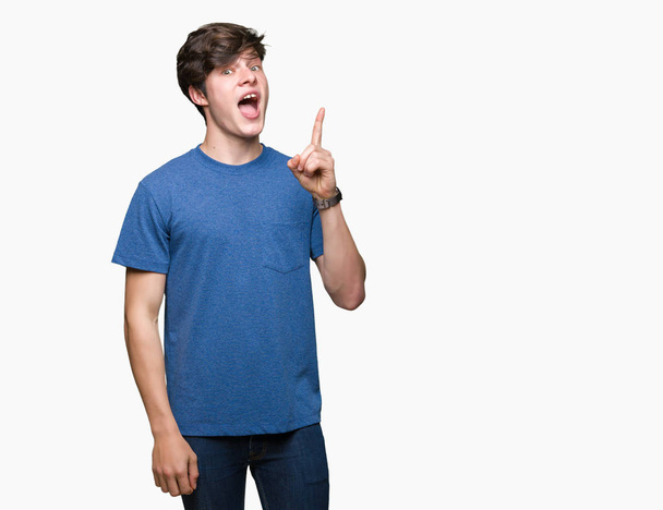 Jonge knappe man met blauw t-shirt over geïsoleerde achtergrond wijzende vinger omhoog met succesvolle idee. Verlaten en gelukkig. Nummer één. - Foto, afbeelding