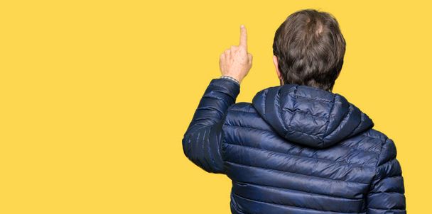 Orta yaş yakışıklı adam giyen kış ceket geriye doğru arkasında parmak eliyle işaret Posing - Fotoğraf, Görsel