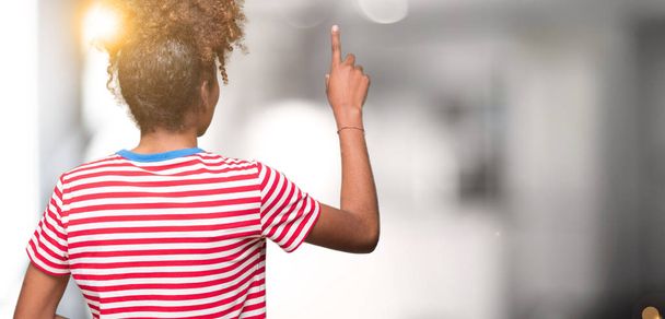 Mooie jonge african american vrouw over geïsoleerd background Posing achteruit wijzende achter met vinger hand - Foto, afbeelding