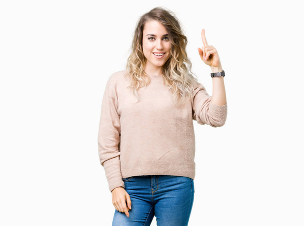 schöne junge blonde Frau in Sweatshirt über isoliertem Hintergrund zeigt mit dem Finger nach oben mit erfolgreicher Idee. aufgeregt und glücklich. Nummer eins. - Foto, Bild