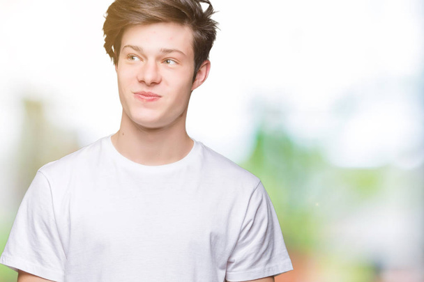 Jonge knappe man dragen casual wit t-shirt over geïsoleerde achtergrond glimlachend uitziende kant en staren weg denken. - Foto, afbeelding