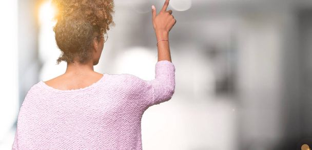 Красивая молодая африканская американка в очках на изолированном фоне, позирует задом наперёд, указывая пальцем на спину.
 - Фото, изображение
