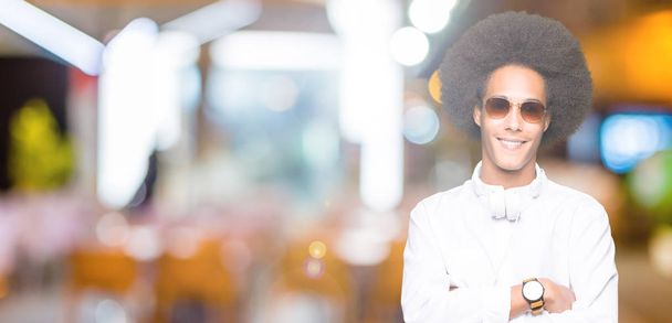 Young african american man with afro hair wearing sunglasses and headphones happy face smiling with crossed arms looking at the camera. Positive person. - Photo, Image