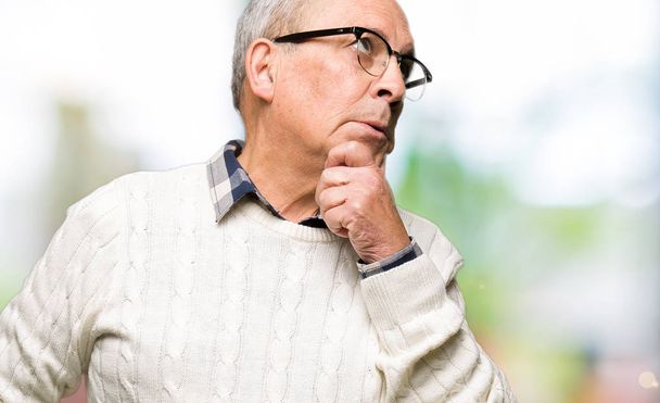 Pohledný starší muž na brýlích a v zimním svetru s rukou na bradě přemýšlí o otázce, zamyšrlivý výraz. Usmívá se zamyšleným obličejem. Koncepce pochybností. - Fotografie, Obrázek