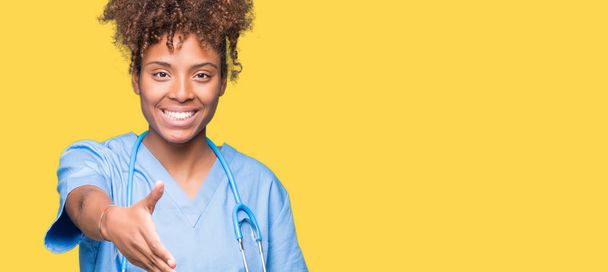 Genç Afro-Amerikan doktor kadın dostu sunan el sıkışma tebrik ve davet edici olarak gülümseyen izole arka plan yüzünden. Başarılı iş. - Fotoğraf, Görsel