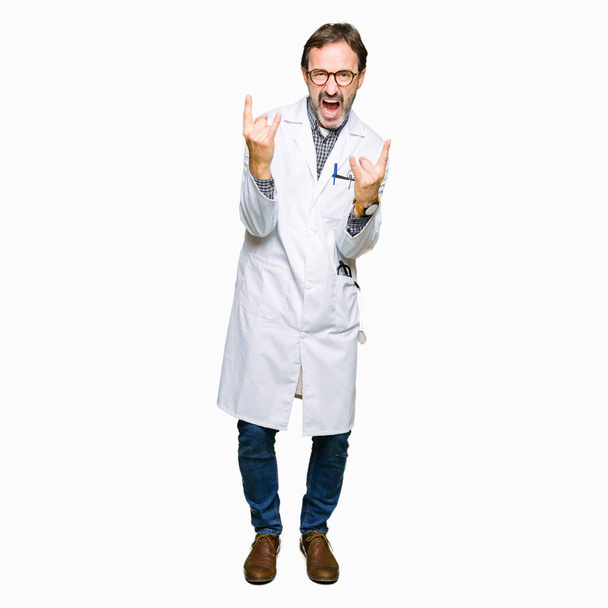 Чоловіки середнього віку лікарі в медичному пальто кричать з божевільним виразом роблять рок-символ з руками вгору. Музична зірка. Важка концепція
. - Фото, зображення