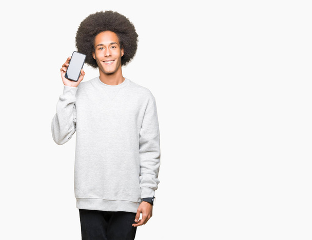 Jonge Afro-Amerikaanse man met afro haar smartphone scherm tonen met een blij gezicht permanent en lachend met een vertrouwen glimlach weergeven tanden - Foto, afbeelding
