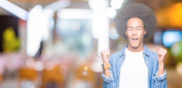 Young african american man with afro hair excited for success with arms raised celebrating victory smiling. Winner concept. - Photo, Image