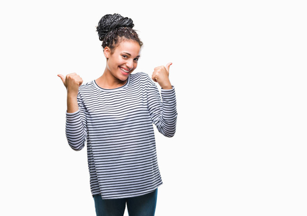 Молодий плетінням волосся афро-американських дівчата носити светр над ізольованих фон успіх знак робить позитивний жест рукою, пальці руки вгору посміхаються і щасливі. Дивлячись на камеру з веселим вираз, переможець жест. - Фото, зображення